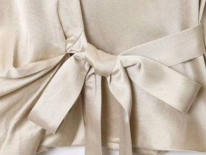 Detailed close-up of champagne gold satin wrap top featuring a side bow tie detail
