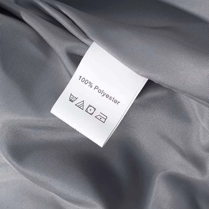 Nahaufnahme des Etiketts einer grauen Polyesterjacke mit Pflegehinweisen und Symbolen