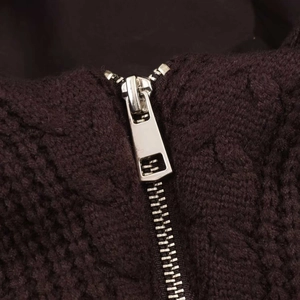 Detailed macro view of the silver metal zipper on dark brown cable knit fabric garment