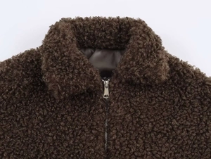 Detail of dark brown teddy fleece jacket featuring soft faux fur texture and silver metal zipper