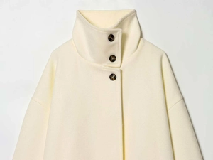 Close-up of cream wool coat with high stand collar and brown tortoise buttons