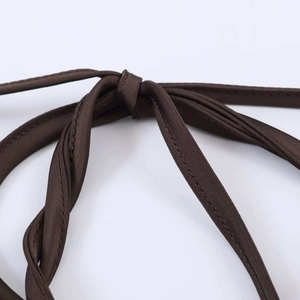 Détail macro d'une bretelle de robe en satin marron foncé avec nœud simple et couture