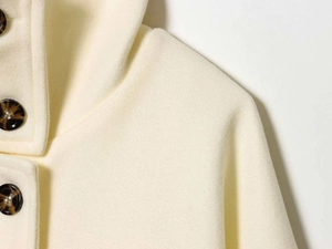 Close-up of cream wool coat detail featuring tortoiseshell button and hood structure