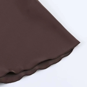 Gros plan sur l'ourlet ondulé et les coutures précises du tissu en satin marron