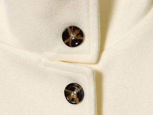 Macro shot of double-sided wool coat detail with tortoiseshell buttons and cream fabric