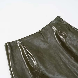 Detail of high-waisted dark green faux leather skirt with glossy finish and zipper