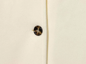 Close-up of a tortoiseshell button on cream wool coat featuring high-quality fabric texture