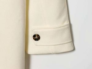 Detail of cream wool coat cuff with decorative strap and tortoiseshell button texture