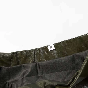 Detail view of glossy dark green leather garment showing size S label and black lining