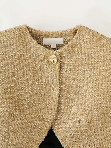 Detail of golden tweed jacket neckline with metallic texture and decorative button