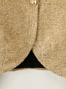 Close-up of golden metallic tweed fabric with intricate weaving and a gold button detail