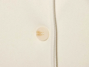 Macro detail of cream wool cape coat featuring an amber resin button and fine stitching