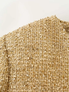 Detail of gold tweed fabric with metallic threads and reflective sequins on short jacket