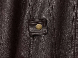 Close-up of deep brown textured leather jacket with vintage brass button and stitching