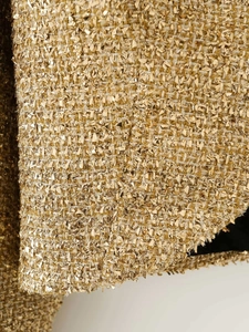 Macro shot of metallic gold tweed fabric with detailed coarse woven texture and black lining