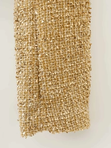 Close-up of golden tweed fabric with intricate 3D weave and metallic fringe texture