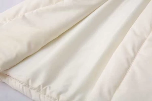 Dettaglio macro del tessuto trapuntato beige con cuciture uniformi per giacca invernale