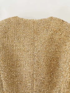 Close-up of golden tweed fabric with metallic glitter threads on a luxury jacket