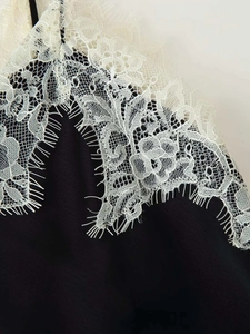Detailed close-up of intricate white eyelash lace stitched on black satin fabric