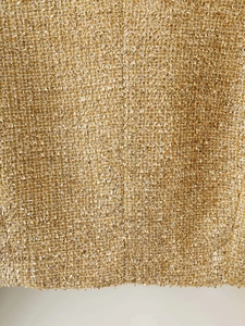 Close-up of golden tweed fabric with metallic yarn and intricate woven texture