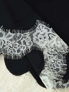 Close-up of delicate white eyelash lace trim with floral patterns on black fabric