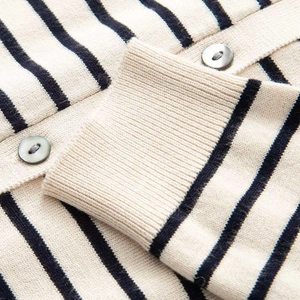 Detailed close-up of striped knit cardigan cuff with glossy shell-textured buttons
