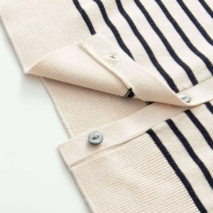 Detailed close-up of striped knit fabric with metallic silver button closure on a beige cardigan
