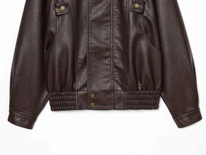 Detail of dark brown leather jacket featuring elastic hem and brass snap button fasteners