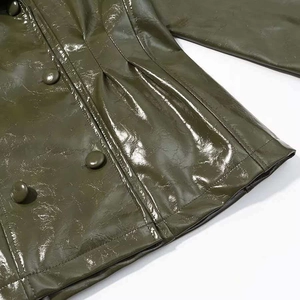 Detail of olive green glossy faux leather jacket with covered buttons and waist pleats