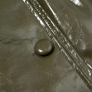 Close-up of olive green glossy leather fabric with matching button and double stitching