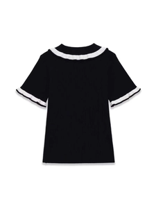 Close-up of black ribbed knit top with contrasting white ruffled neckline and sleeves
