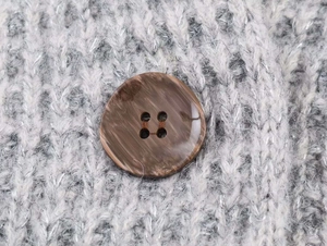 Détail d'un bouton marbré marron à quatre trous sur le tissu d'un cardigan en maille grise