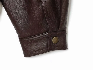 Detail of dark brown leather jacket sleeve showing bronze snap button and stitch texture