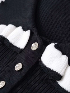 Detail of knit cardigan with white ruffled trim and sparkling crystal-embellished button
