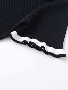 Close-up of black ribbed knit fabric with delicate white wavy lettuce edge detailing