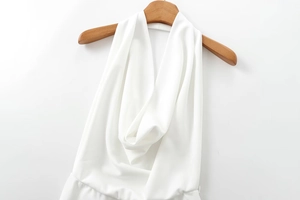Detailed view of white halter neck crepe jumpsuit with deep V-neckline on wooden hanger