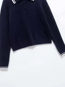 Detailed view of dark knit polo shirt with white contrast stripes on collar and cuffs