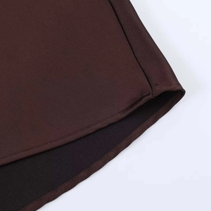 Detail view of the curved hem design on a dark brown satin texture midi dress