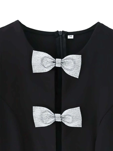 Détail de la robe noire avec deux nœuds en strass argentés et col rond sur fond blanc