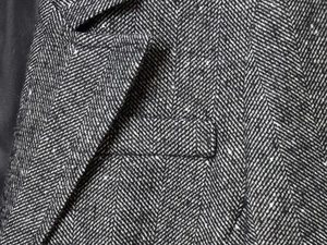 Macro shot of grey herringbone blazer showing detailed tweed texture and flap pocket detail