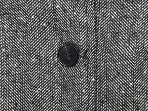 Detail of grey herringbone wool fabric with a matte black four-hole button on the blazer
