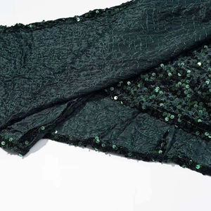 Detail of dark green dress fabric with intricate pleats and sparkling sequin trim