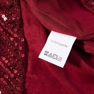 Detail view of burgundy sequin dress fabric and 100% polyester care label