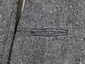 Close-up of the grey herringbone tweed fabric texture and welt pocket of the blazer