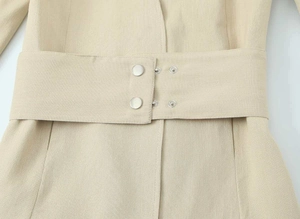 Detail eines hellbeigen Blazers mit strukturiertem Stoff, breitem Taillengürtel und Druckknopf