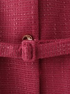 Dettaglio della trama in tweed rosa con bottone metallico dorato e rifiniture del bordo