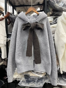 Dettaglio di un cardigan grigio chiaro con cappuccio, fiocco marrone e chiusura a zip