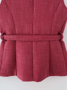 Dettaglio macro del gilet in tweed lampone con trama intrecciata e cintura abbinata