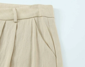 Detailaufnahme der beigen Hose mit Leinentextur, Taillenfalten und seitlichen Taschen