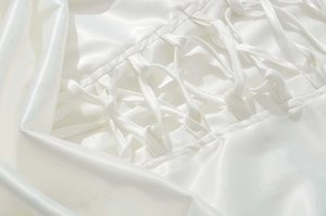 Détail macro du laçage croisé au dos d'une robe en satin blanc avec texture soyeuse
